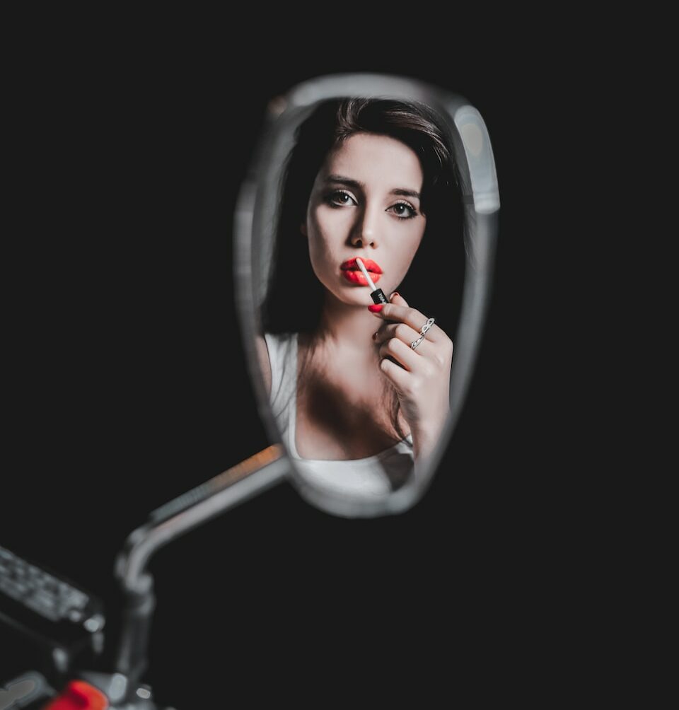 woman applying lipstick in front of wing mirror